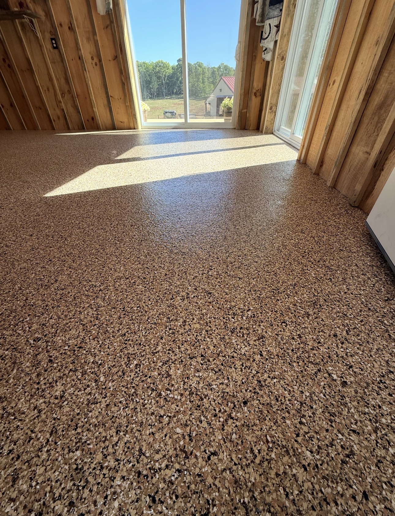 Tan full-broadcast flake floor coating in a bright wood-framed room